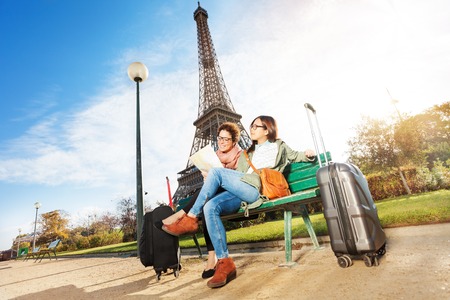 Two happy friends, female tourists, reading map sitting on the bench near the Eiffel Tower in Parisの写真素材