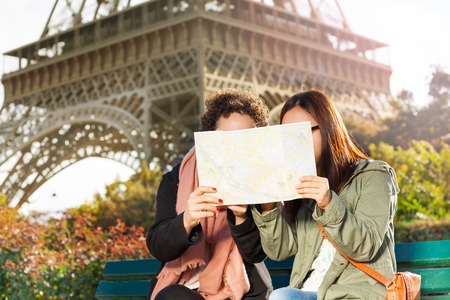 Two women sitting on a bench and looking at a paper map during their excursion in Parisの写真素材
