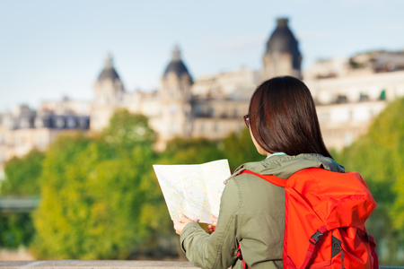 Young girl with big red backpack looking to the traveler guide book of Parisの写真素材