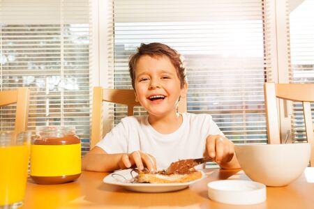 Happy boy spreading chocolate with knife on toastの写真素材