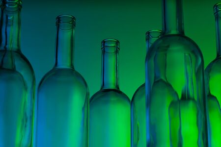 Group of clear glass wine bottles in green lightの写真素材