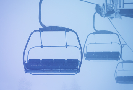 Empty cabins of chairlift on ropeway in thick fogの写真素材