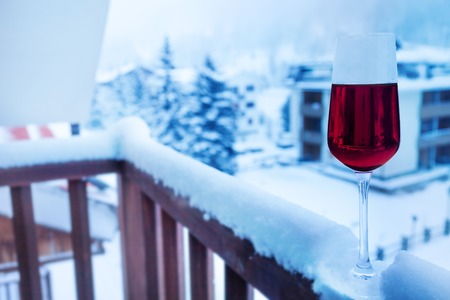 A glass of cold red wine on the snow-cowered balcony balustrade of hotel suiteの写真素材