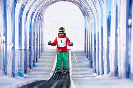 Little boy going uphill under transparent safety archway using ski liftの写真素材