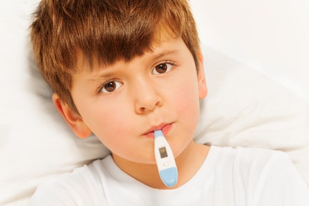 Boy taking temperature with electronic thermometerの写真素材