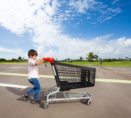 Kid boy pushing empty shopping cart at parking lotの写真素材