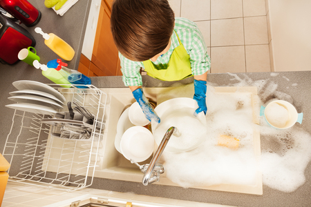 Boy rinsing dishes in the sink full of soap sudsの写真素材