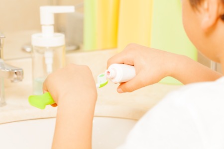Kid spreading toothpaste on green toothbrushの写真素材