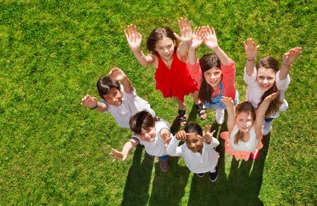 Happy kids standing on grass and waving handsの写真素材