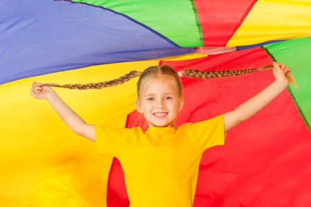 Cute little girl with two braids standing under the tent made of colorful parachuteの写真素材