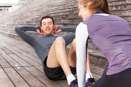 Young man making abs exercises outdoors with coach