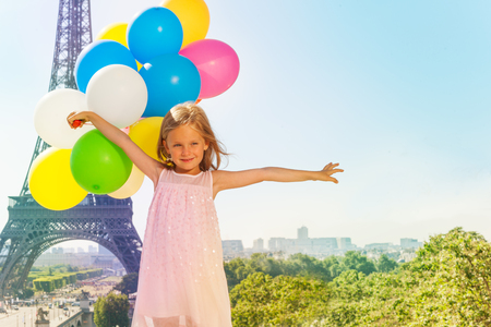 Portrait of five years old girl wearing pink dress, holding colorful balloons bouquet, against the Eiffel Tower background with copy-spaceの写真素材