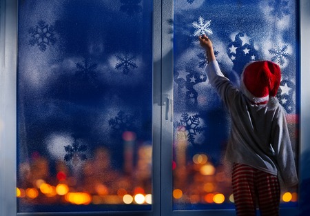 Boy decorate window for New Year with snowflakeの写真素材