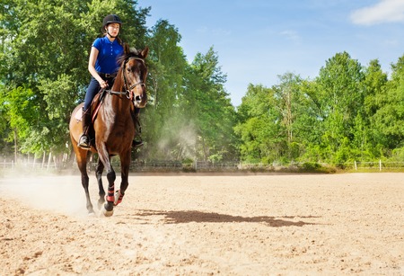 Young woman riding bay horse at sand racetrackの写真素材