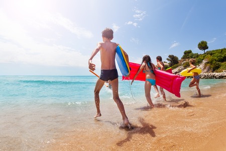 Group of kids run into the sea on sunny beachの写真素材