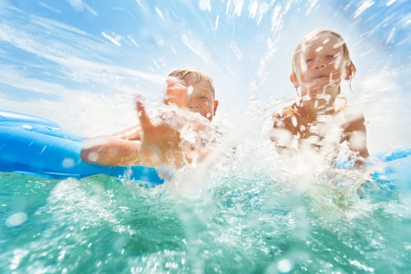Two boys splashing in the sea while swimmingの写真素材
