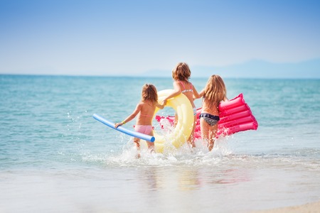 Three girls with swimming tools running to the seaの写真素材