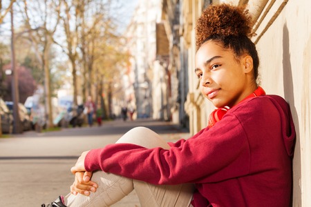 African preteen girl sitting alone at sidewalkの写真素材