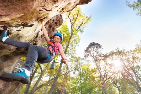 Bottom view of teenage rock climber exercising in the forest area against blue sky with copy-spaceの写真素材