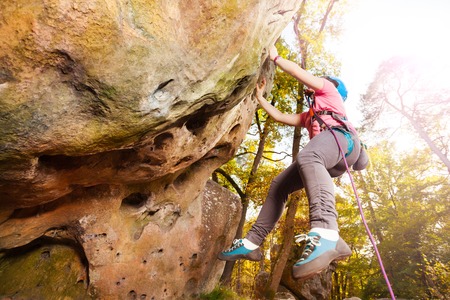 Girl climbing on a rock against autumn forestの写真素材