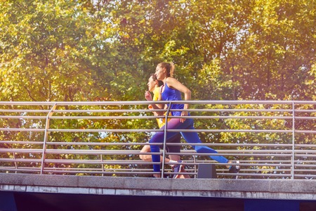 Young couple running across a bridge at city parkの写真素材