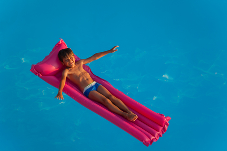 Happy boy relaxing on inflatable mattress in poolの写真素材