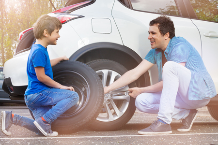 Happy father and son changing wheels on carの写真素材