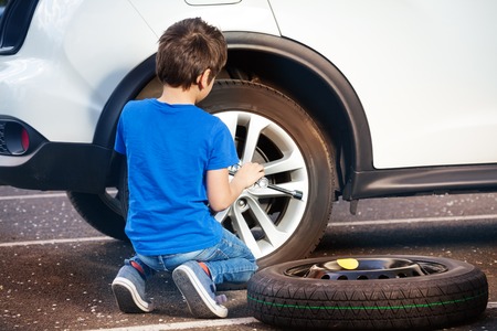 Boy learning how to change tyre using wheel braceの写真素材