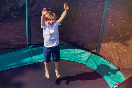 Excited boy bouncing on the trampoline outdoorsの写真素材