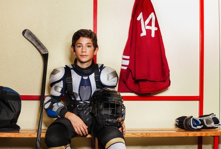 Boy sitting on the bench in ice hockey locker roomの写真素材
