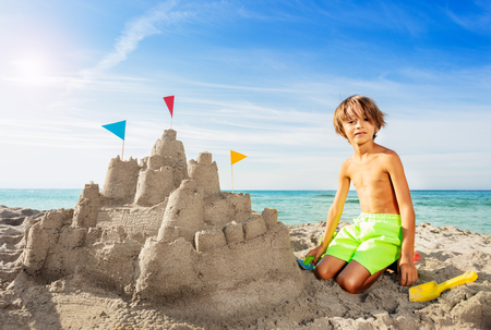 Happy boy building big sand castle on the beachの写真素材