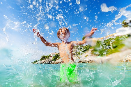 Excited boy having fun splashing water in the seaの写真素材