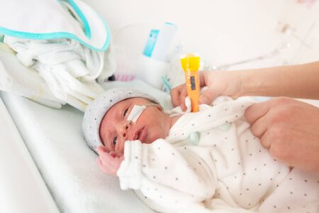 Premature born infant in ICU with thermometer