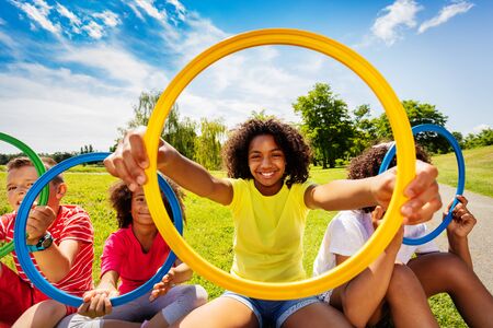 Girl in group of kids look through colorful hoopの写真素材