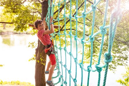 Boy climbing net high on tree at adventure parkの写真素材