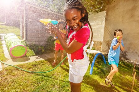 Girl with group of kids play water pistol fightの写真素材