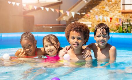 Four kids play in backyard swimming pool togetherの写真素材