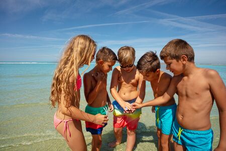 Group of kids circle to check out found seashells