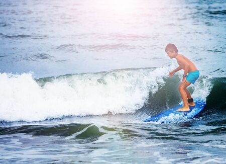 Little boy in surfing school learn to surf waves in the sea standing on the board