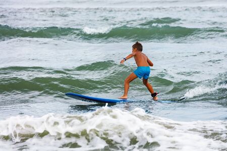Little boy learning to surf in the stand on board surfing small waves