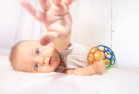 Little infant baby stretch with hand to the camera laying on the side on the bed