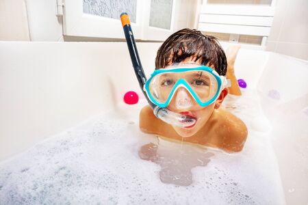 Little cute boy swim and dive in the bathtub wear snorkeling mask, scuba smiling play with soap...