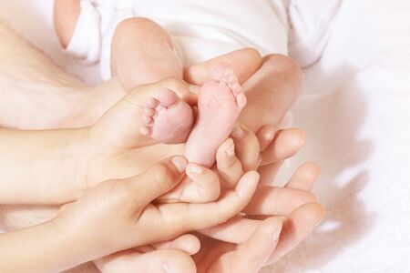 Many hands adult and children mother with brother hold infant tiny baby feet