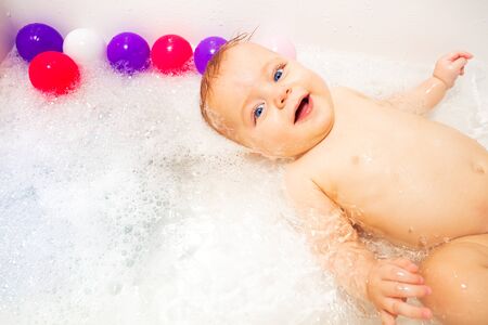 Baby in bath tub bathroom with soap swim in water happy smiling laying on back look upの写真素材