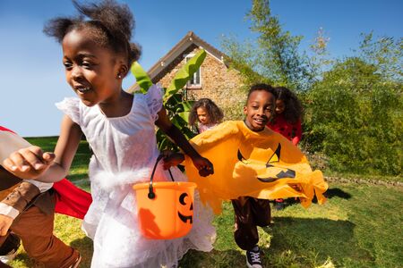 Close portrait of a group of little children run in Halloween costume on the lawn before the house holding handsの写真素材