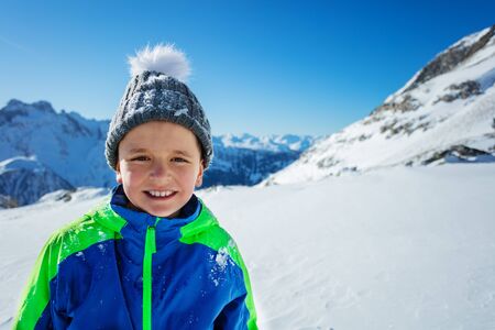 Happy boy in winter hat walking in sunny mountains close smiling portrait with copy spaceの写真素材