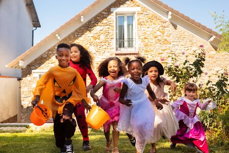 Close portrait of a group of kids run in Halloween costume on the lawn before the house together, screaming with candy bucketsの写真素材