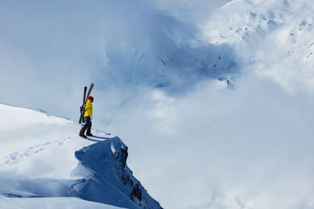Adult man stand on the mountain top cliff with backpack and ski observe long alpine panorama to...