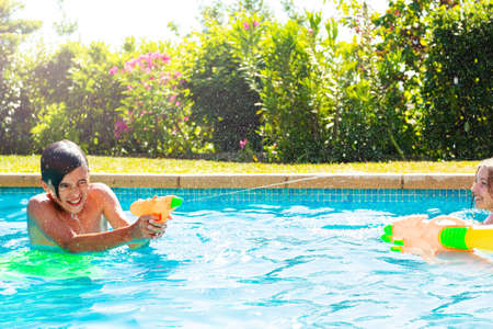 Boy in swimming pool shooting with water squirt gun on sunny summer day
