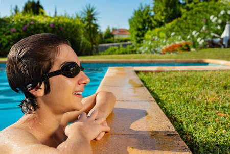 Happy handsome boy on the border of swimming pool wear swim goggles and smile looking aside
